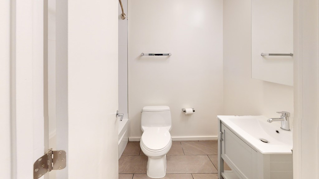 A clean, minimalistic bathroom featuring a toilet, a bathtub, and a vanity with a sink. The room has a calm, orderly vibe.