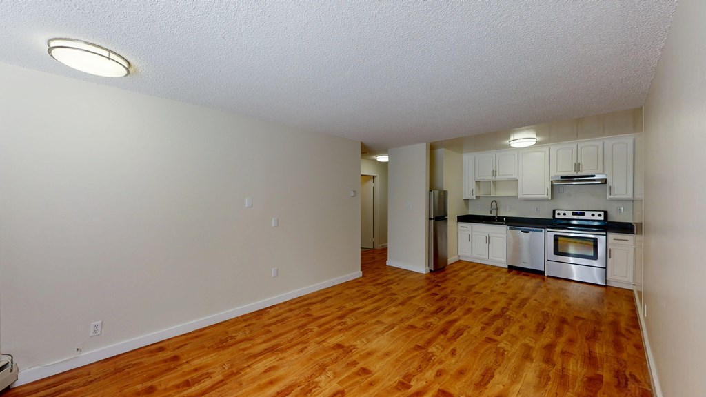 A kitchen with white cabinets and stainless steel appliances is visible from the living room.
