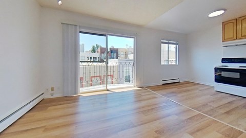 Well-lit living room with a wood-like floor, a sliding glass door that leads to a balcony, and a view of the kitchen Well-lit living room with a wood-like floor, a sliding glass door that leads to a balcony, and a view of the kitchen