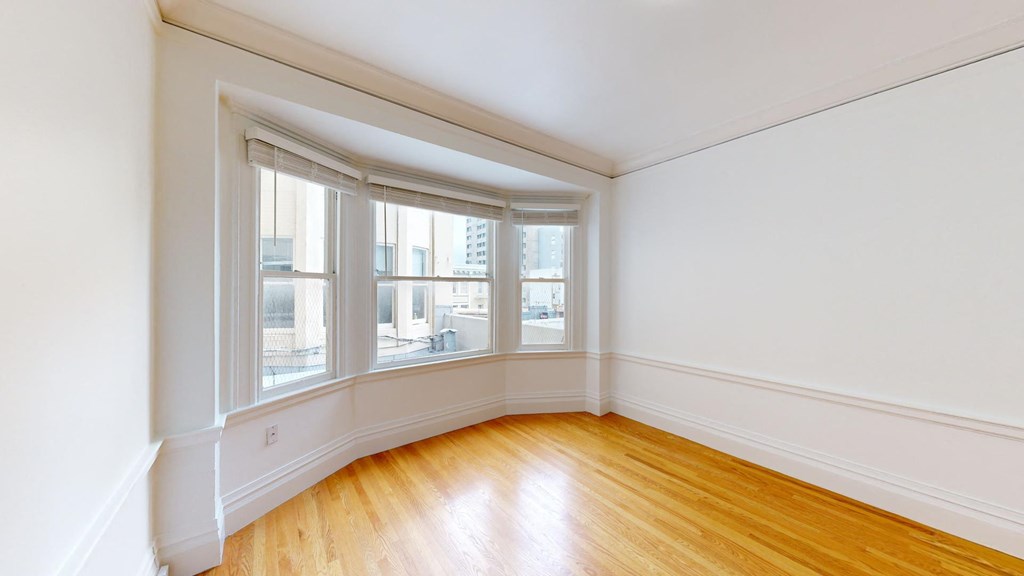 a bedroom with white walls and a window and wood floors