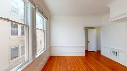 A room with white walls and wooden floors with a window on the left.