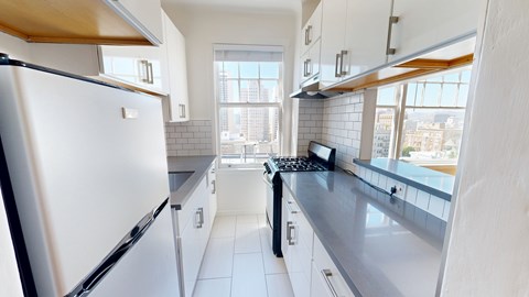 A white refrigerator is in a kitchen with white cabinets and a black stove.
