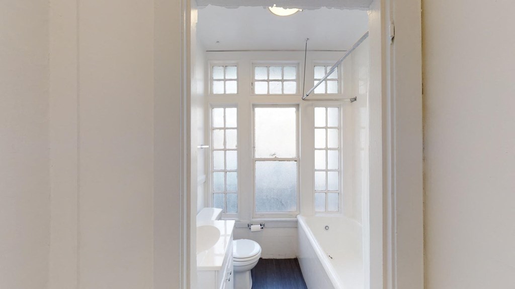 a white bathroom with a window and a toilet and a tub