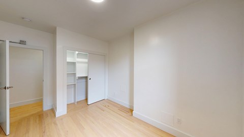 A spacious, minimally furnished room featuring wood floors, a closet. Brightly lit and clean.