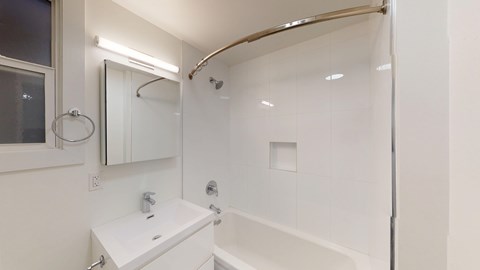 A modern bathroom featuring a bathtub, sleek sink, large mirror, and a curved shower rod with a glass enclosure.