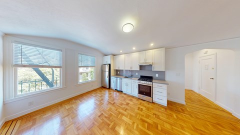 A spacious kitchen with wooden floors and white cabinetry.