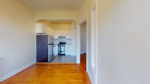 A kitchen with a refrigerator, oven, and sink is visible through a doorway.