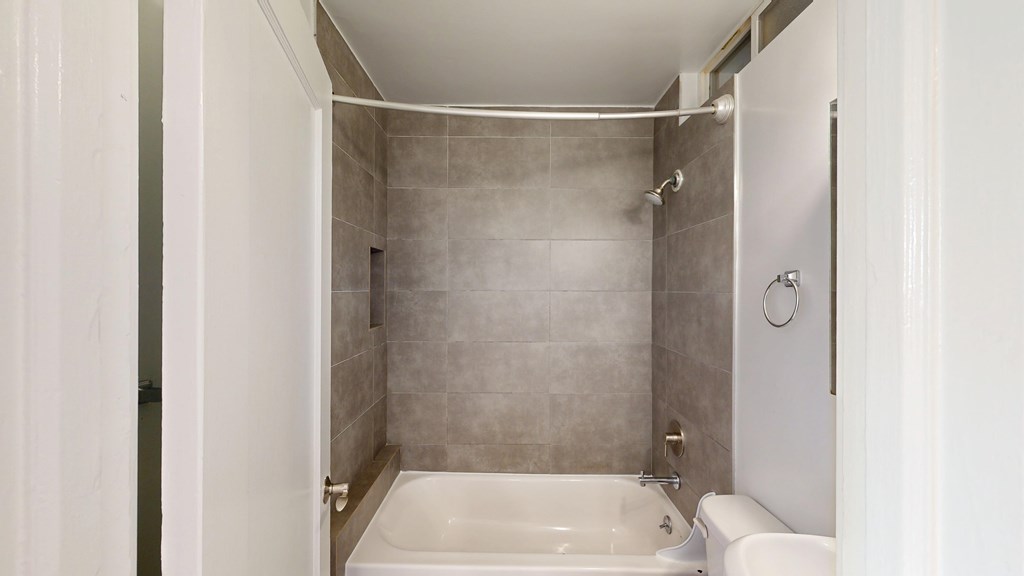 A bathroom with a white tub and grey tiles.
