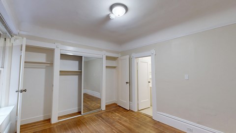 A room with a white ceiling and wooden floors with a mirror on the wall.