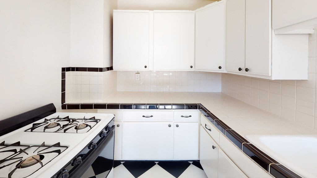 A modern kitchen with white cabinets and a black and white checkered floor.