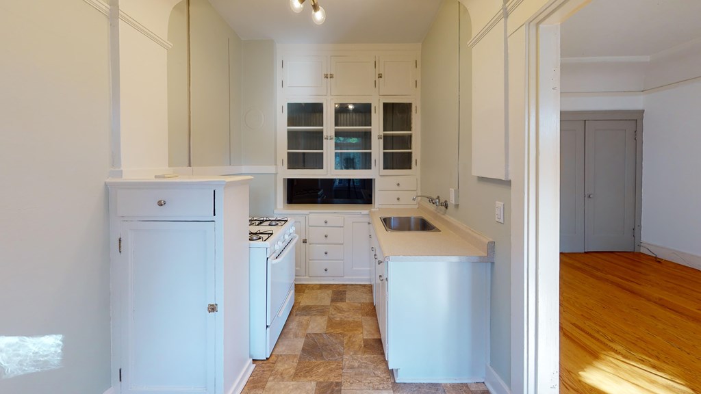 Kitchen with cabinets, gas stove, stainless sink, and glass-front storage