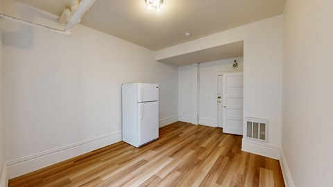 A white refrigerator in a room with wooden floors and white walls.