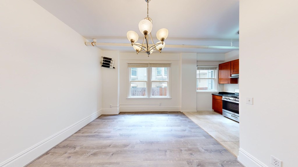 A well-lit, empty living room with a chandelier and a kitchen in the background.