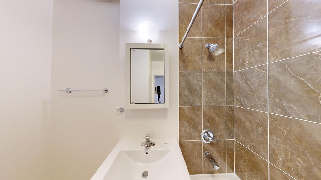 A bathroom with a white tub and a mirror above it.