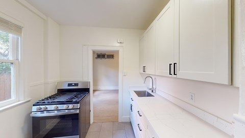 A kitchen with a stove, sink, and cabinets.