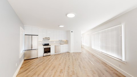an empty living room with a large window and a kitchen
