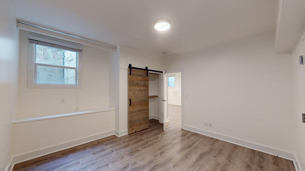 a bedroom with white walls and wood floors and a sliding barn door