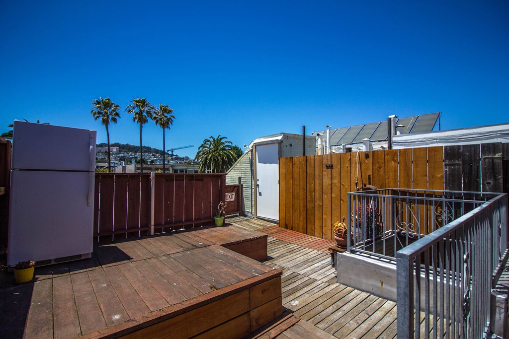 a rooftop deck with a refrigerator and a fence and palm trees