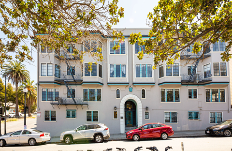 A red car is parked in front of a white building with a green door.