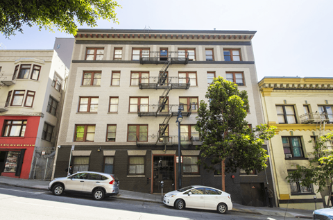 A white car is parked on the street in front of a building with a fire escape.