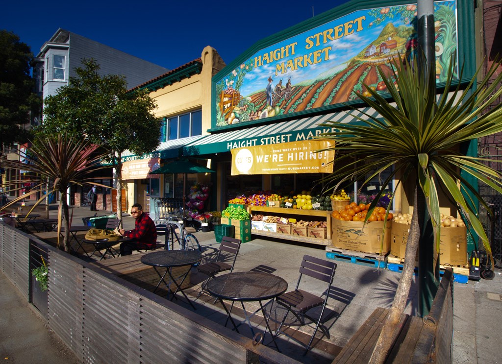 a street scene with tables and chairs outside of a fruit market