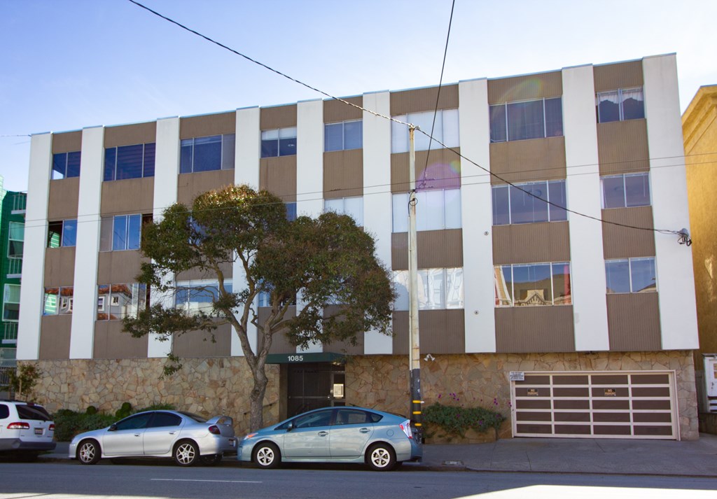 Two cars parked in front of a building with a tree in front of it.