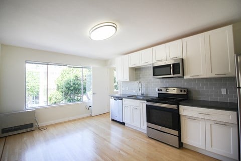 an empty kitchen with white cabinets and appliances and a window