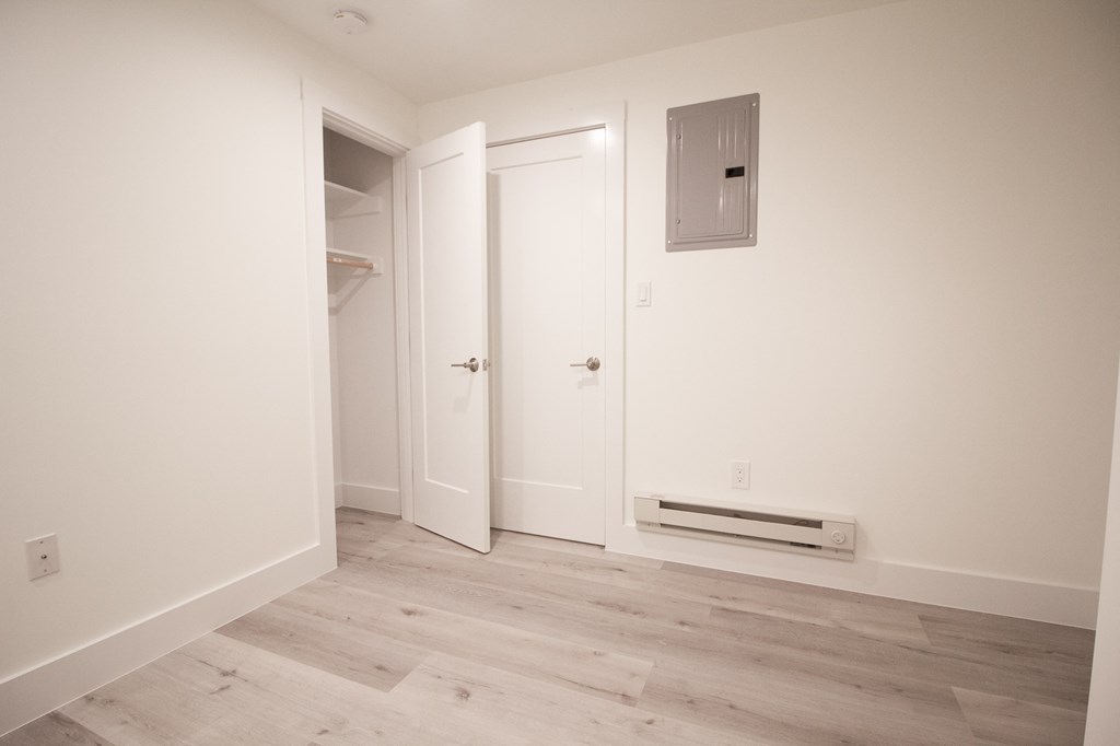 a bedroom with white walls and wood floors and a closet