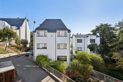 A white building with a black roof is surrounded by greenery and a clear blue sky.
