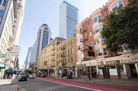 A city street with a mix of old and new buildings, cars on the road, and a pedestrian crossing.