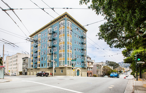 A blue and yellow building is situated on a street corner with cars parked on the side of the road.