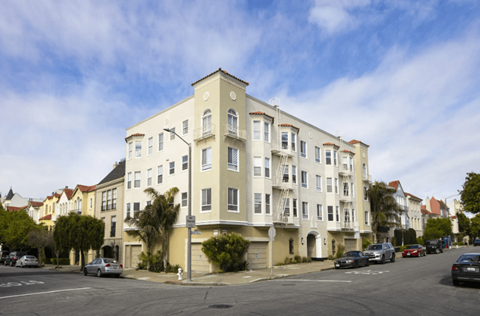 A street view of a white building with cars parked in front.
