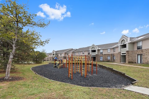 A playground with a swing set in the middle of a gravel area in front of apartment buildings. at Eagles Edge Apartments, Indianapolis, IN 462542
