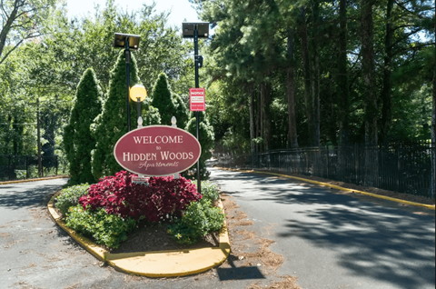 A sign that says "Welcome to Hidden Woods" is in front of a street.