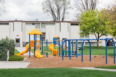 A playground with a yellow and blue slide in front of a building.