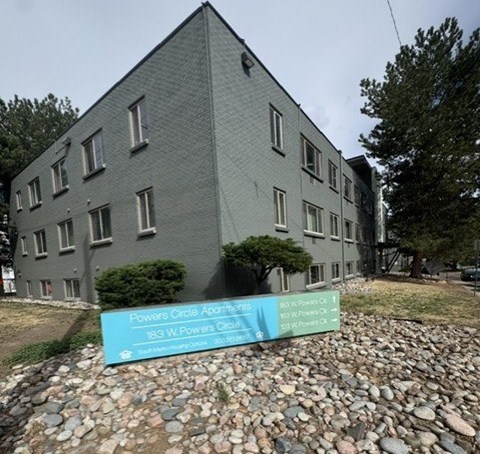 A grey building with a sign in front that says Powers Circle Apartments.