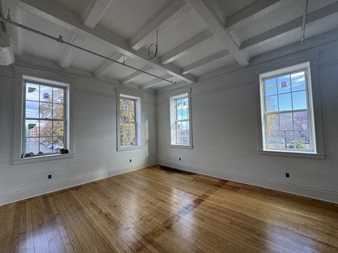 A room with wooden floors and three windows.