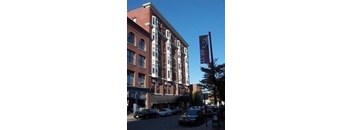 A tall building with a red brick facade stands next to a tree.