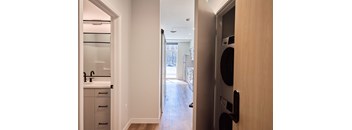 A modern kitchen with a wooden door and a view of the hallway.