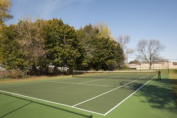 A tennis court surrounded by trees and a fence.