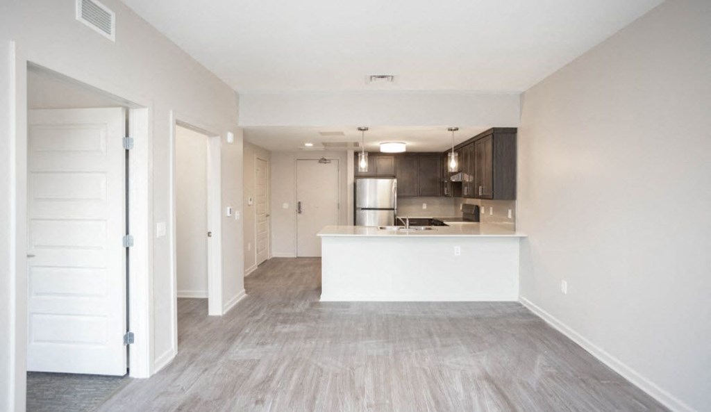 an empty living room and kitchen with white walls and wood flooring
