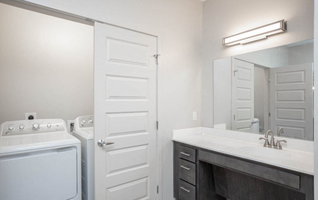 a white washer and dryer in a bathroom with a sink and a mirror