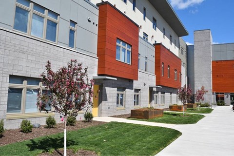 A modern building with a red and grey facade and a green lawn in front.