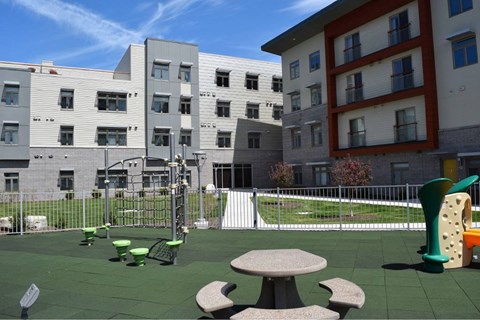 A playground with a green slide and a red and white building in the background.