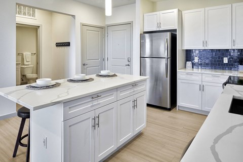 a kitchen with white cabinets and a large island with a stainless steel refrigerator