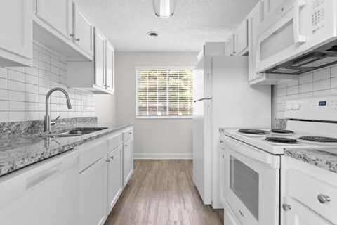 A kitchen with white cabinets and a marble countertop.