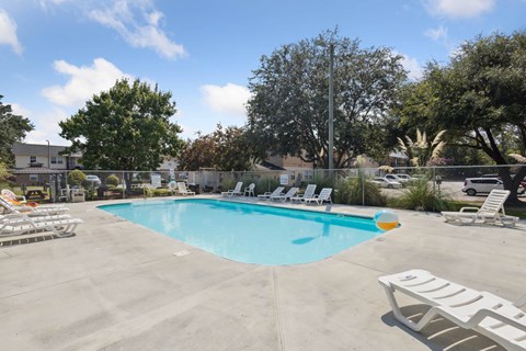 A pool with chairs around it and trees in the background.
