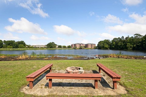 Lakeside fire pit area with wooden benches at Seasons Apartments, Statesboro