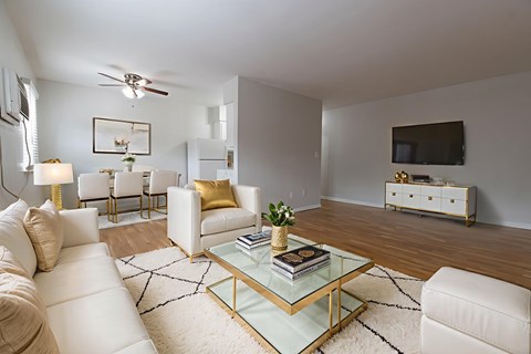 A living room with a white couch, a glass coffee table, and a television on the wall.