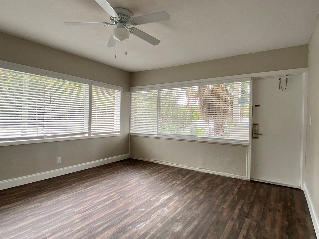 an empty living room with a ceiling fan and large windows